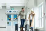 A woman and a man walk beside each other smiling in YFC’s departures hallway. The woman is holding a cowgirl hat and luggage.