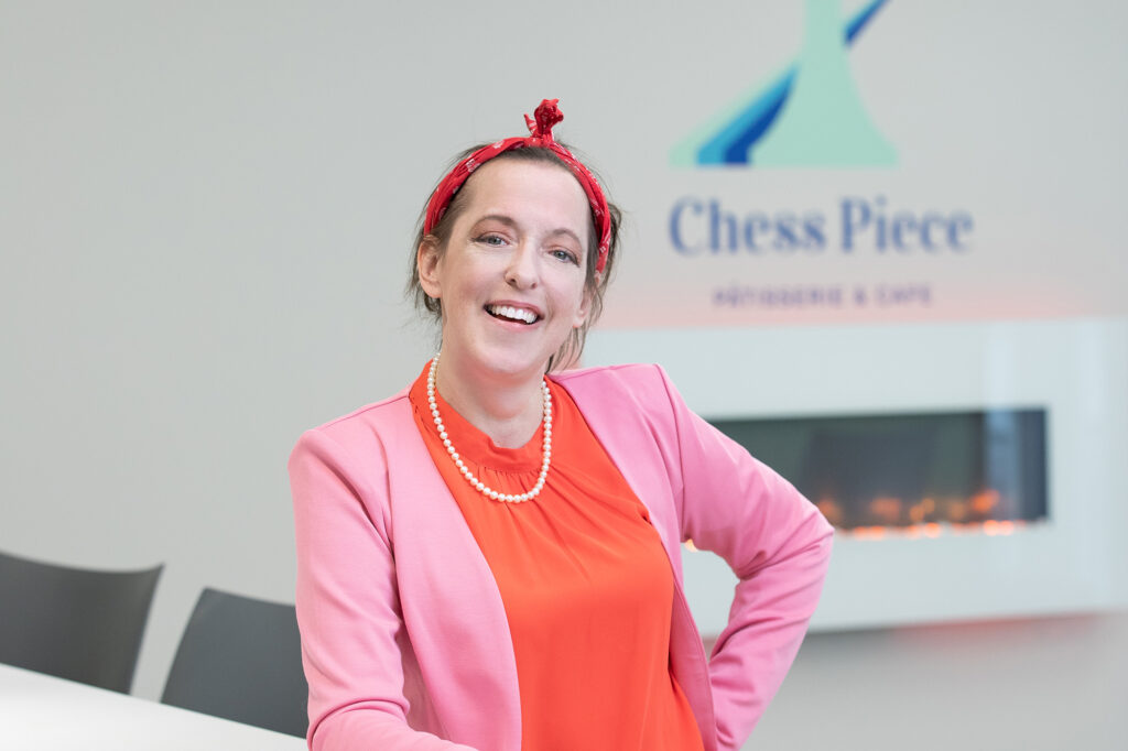 Patti Hollenburg, Owner of Chess Piece Patisserie and Cafe, stands in front of the Chess Piece logo.