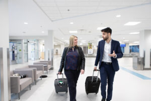 A woman and a man dressed in business attire walk towards the camera pulling two suitcases.