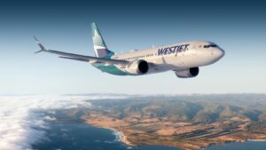 A WestJet plane soars in a blue sky, with breathtakingly beautiful mountains and water below its wings.